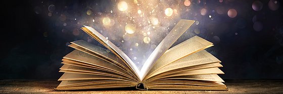 Aus einenm aufgeschlagenen Buch steigen magische Lichter auf.