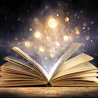 Aus einenm aufgeschlagenen Buch steigen magische Lichter auf.