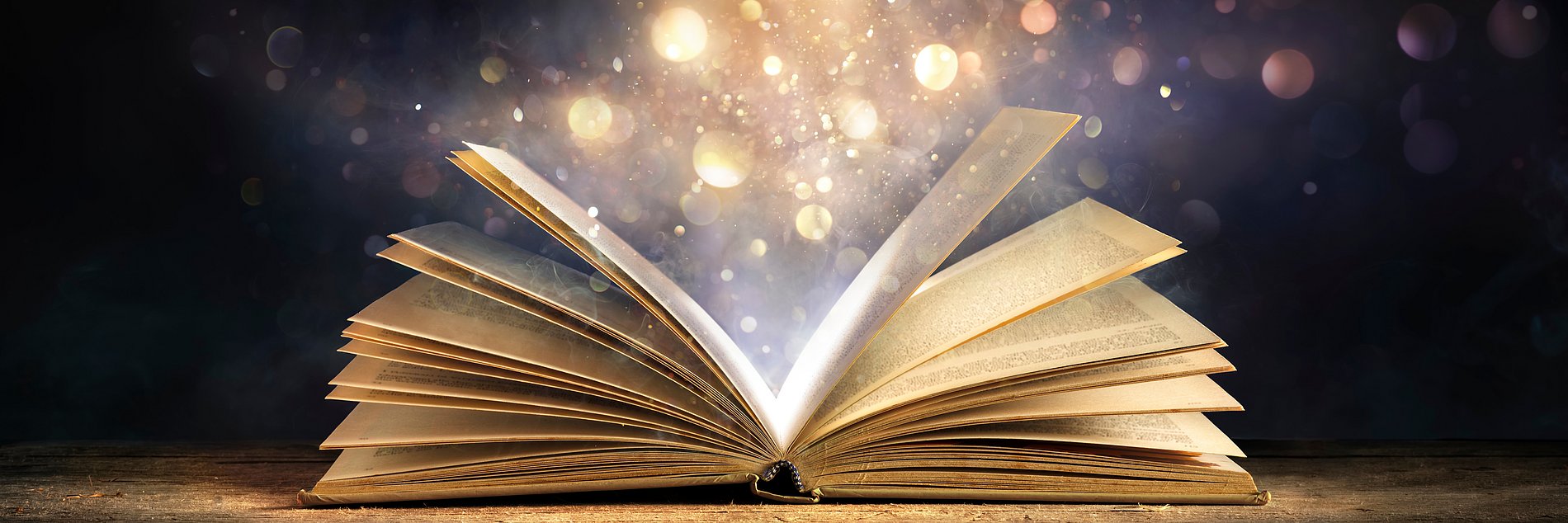 Aus einenm aufgeschlagenen Buch steigen magische Lichter auf.