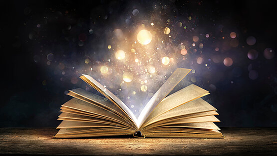 Aus einenm aufgeschlagenen Buch steigen magische Lichter auf.